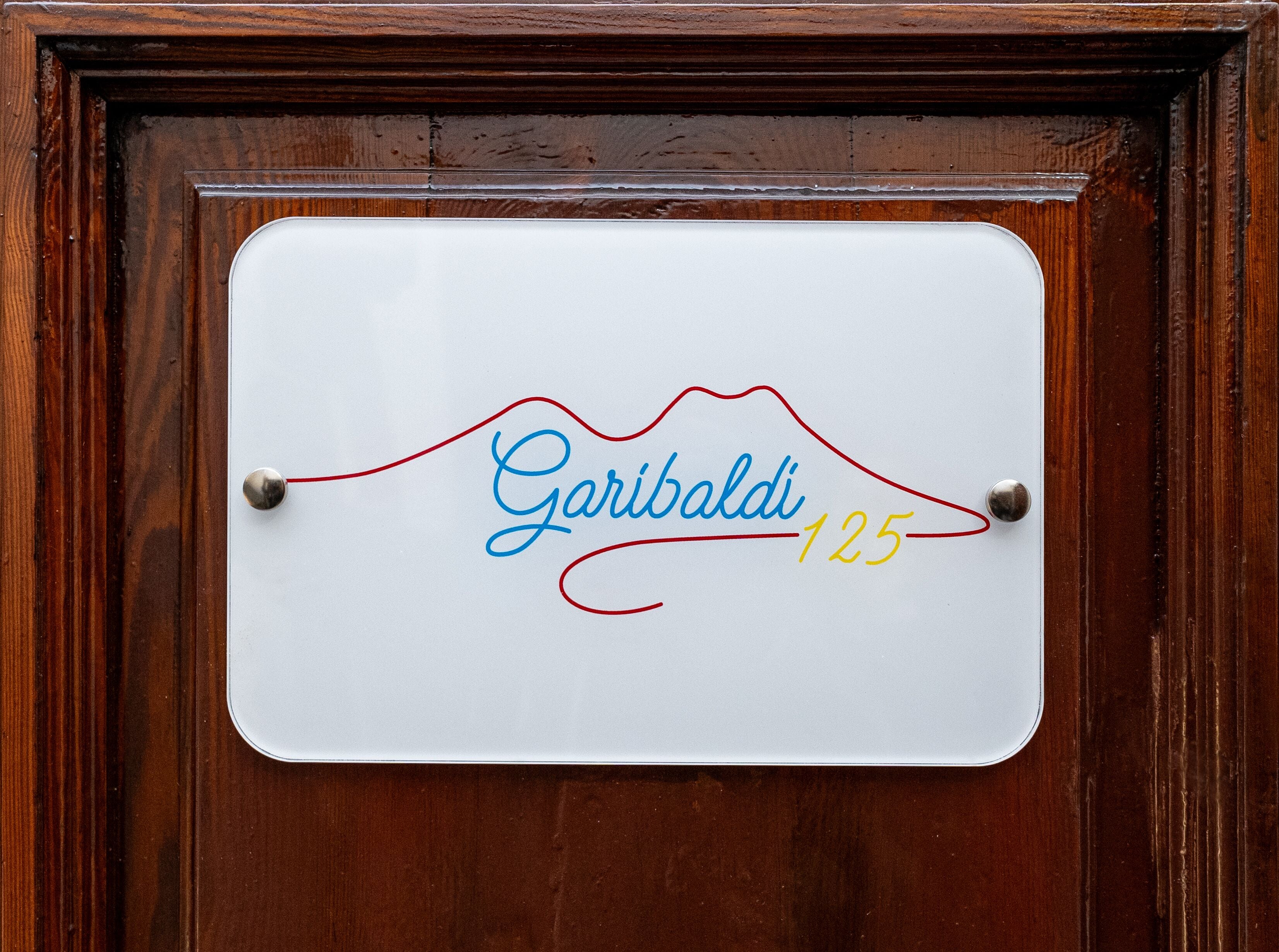 Ein weißes Schild mit dem Namen "Garibaldi" und der Nummer "125" an einer Holztür.