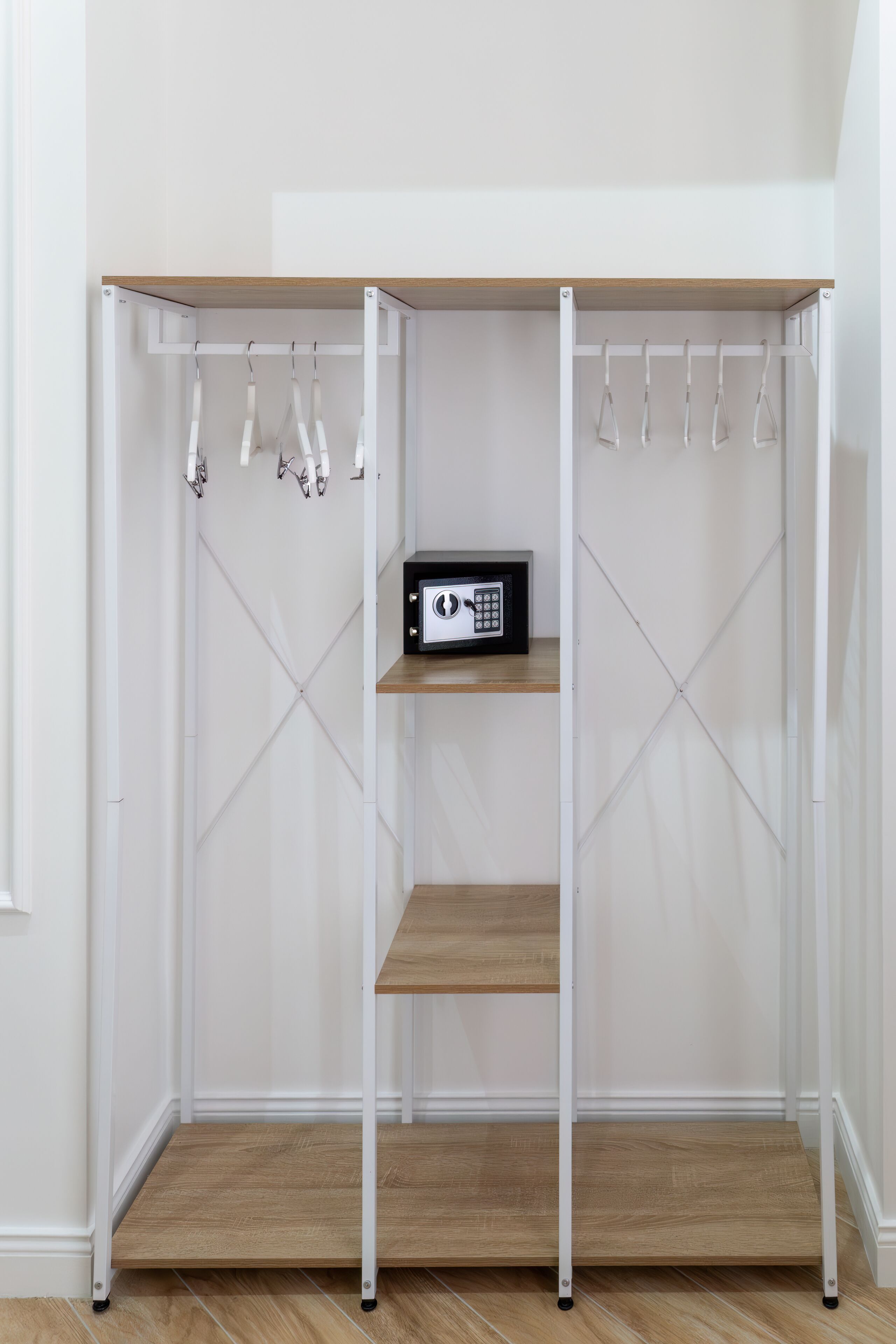 Un armario metálico blanco con microondas en el estante superior, repisas de madera y una barra para colgar ropa.