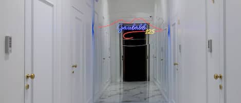A hallway with white walls, marble flooring, and doors with brass handles.