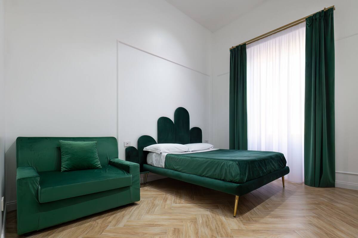 A room with a bed, a green sofa, and a window with curtains.