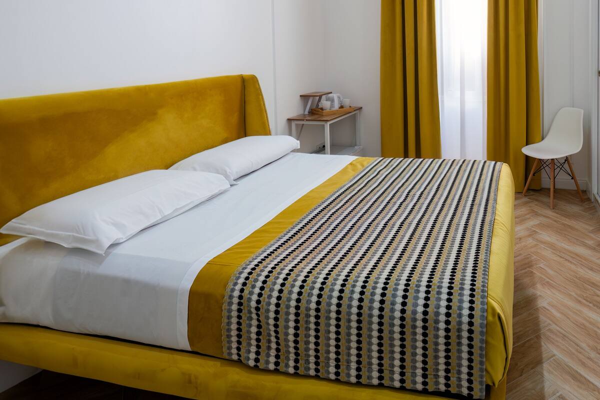 A room with a bed, a small table, a chair, and a window with curtains.