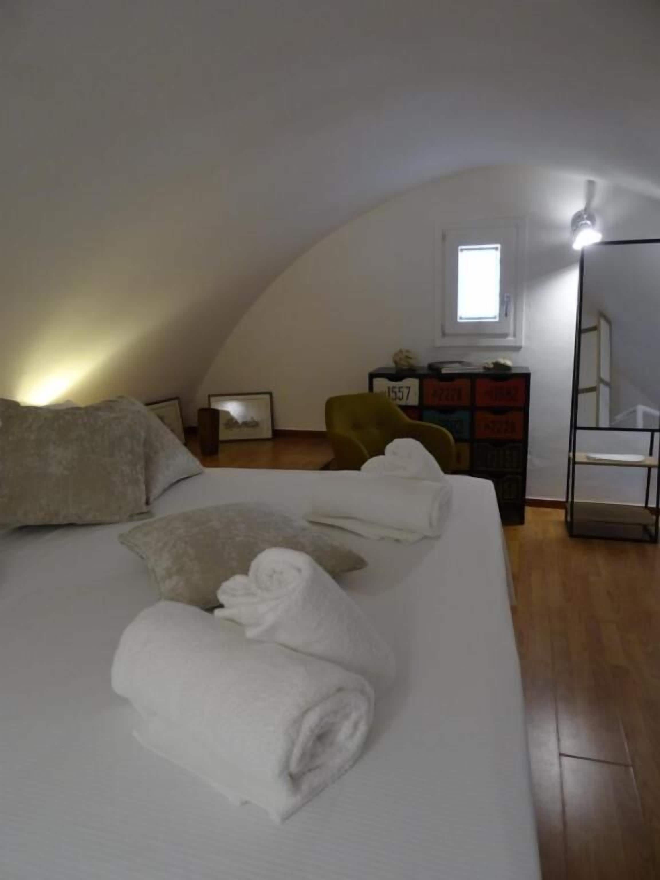 A bedroom with a large bed, a dresser, a chair, and a small window.
