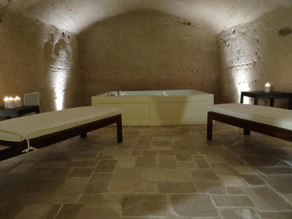 Una habitación con suelo de piedra, una bañera grande, dos mesitas de noche y un banco.