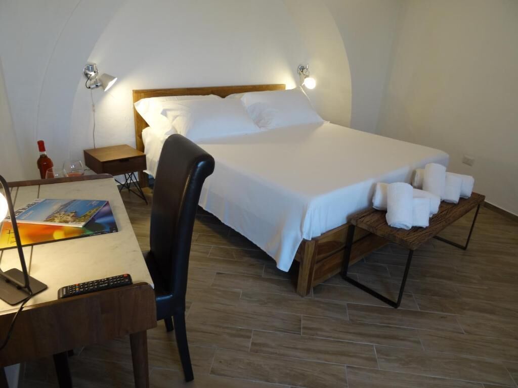 Quarto com cama, mesas de cabeceira, uma cadeira, escrivaninha com abajur e controle remoto.