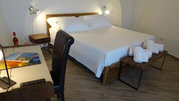 Quarto com cama, mesas de cabeceira, uma cadeira, escrivaninha com abajur e controle remoto.