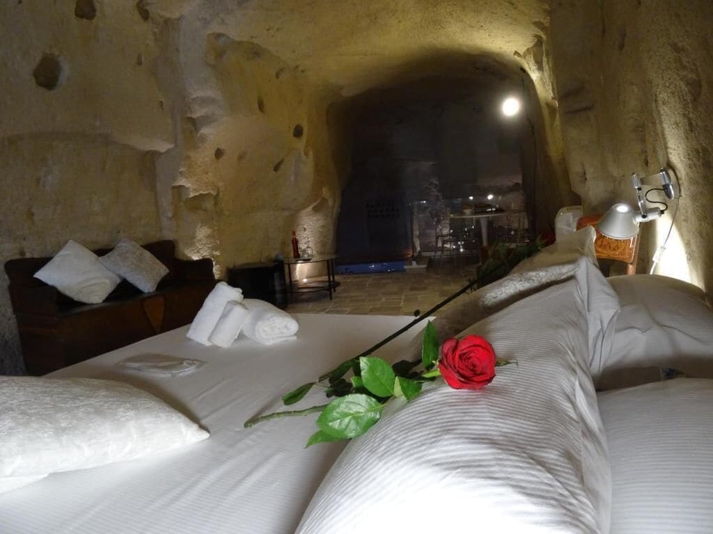 A room with a bed, pillows, a red rose, and a lamp.