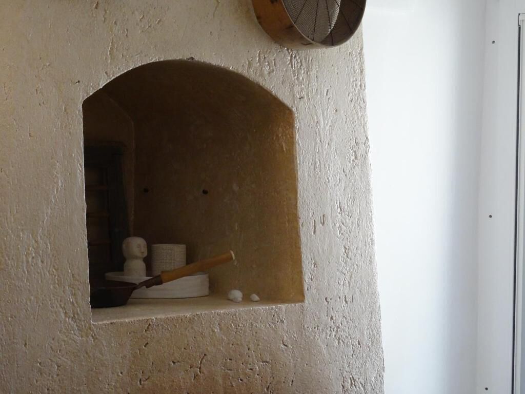 A small arched window with a rustic interior, including a wooden spoon, a bowl, and some white objects.