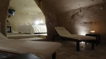 A cozy, cave-like bedroom with a bed, a lounge chair, and a small table.