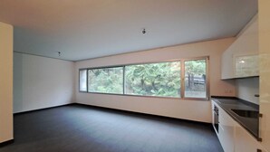 Ein geräumiger Raum mit großem Fenster, dunklem Bodenbelag und moderner Einrichtung.