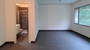 Ein geräumiges, modernes Zimmer mit großem Fenster, Duschbereich und sichtbarer Toilette.