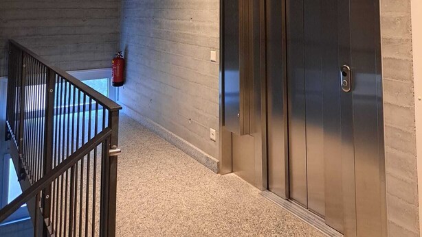 Ein Flur mit einer Betonwand, einem Metallgeländer einer Treppe und einem Feuerlöscher an der Wand.
