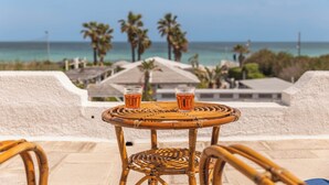 Une table en osier, sur laquelle reposent deux verres contenant un liquide ambré, donnant sur une plage bordée de palmiers et surplombant un ciel dégagé.