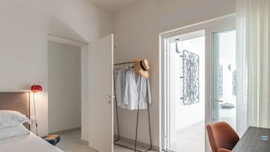 Une chambre d’hôtel moderne équipée d’un lit, d’une table de chevet, d’une lampe de lecture, d’un porte-vêtements et d’un coin repas avec une table et des chaises.