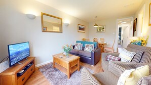 A living room with a sofa, a coffee table, a TV, and a dining area with chairs and a table. - Pine Marten Cottage Aviemore  | Cosy Holiday Cottage in Silverglades (Aviemore)