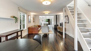 Una sala de estar moderna con piso de madera oscura, una mesa de comedor redonda, un sofá y una escalera con barandillas blancas.