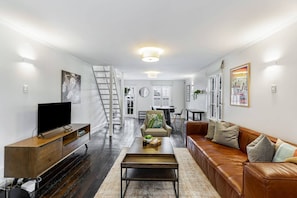 Ein modernes Wohnzimmer mit Fernseher, einer Holz-Unterhaltungsecke, einer Ledersofa und einer Treppe, die zu einer oberen Etage führt.