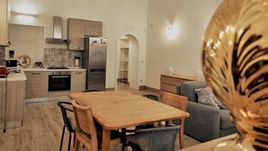 A modern kitchen with stainless steel appliances, a dining area with a wooden table and chairs, and a grey sofa in the living area. - Athena Apartment Ortigia Holidays (Siracusa)