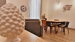 A modern dining area with a wooden table and chairs, a decorative white sculpture, and a wall clock. - Athena Apartment Ortigia Holidays (Siracusa)