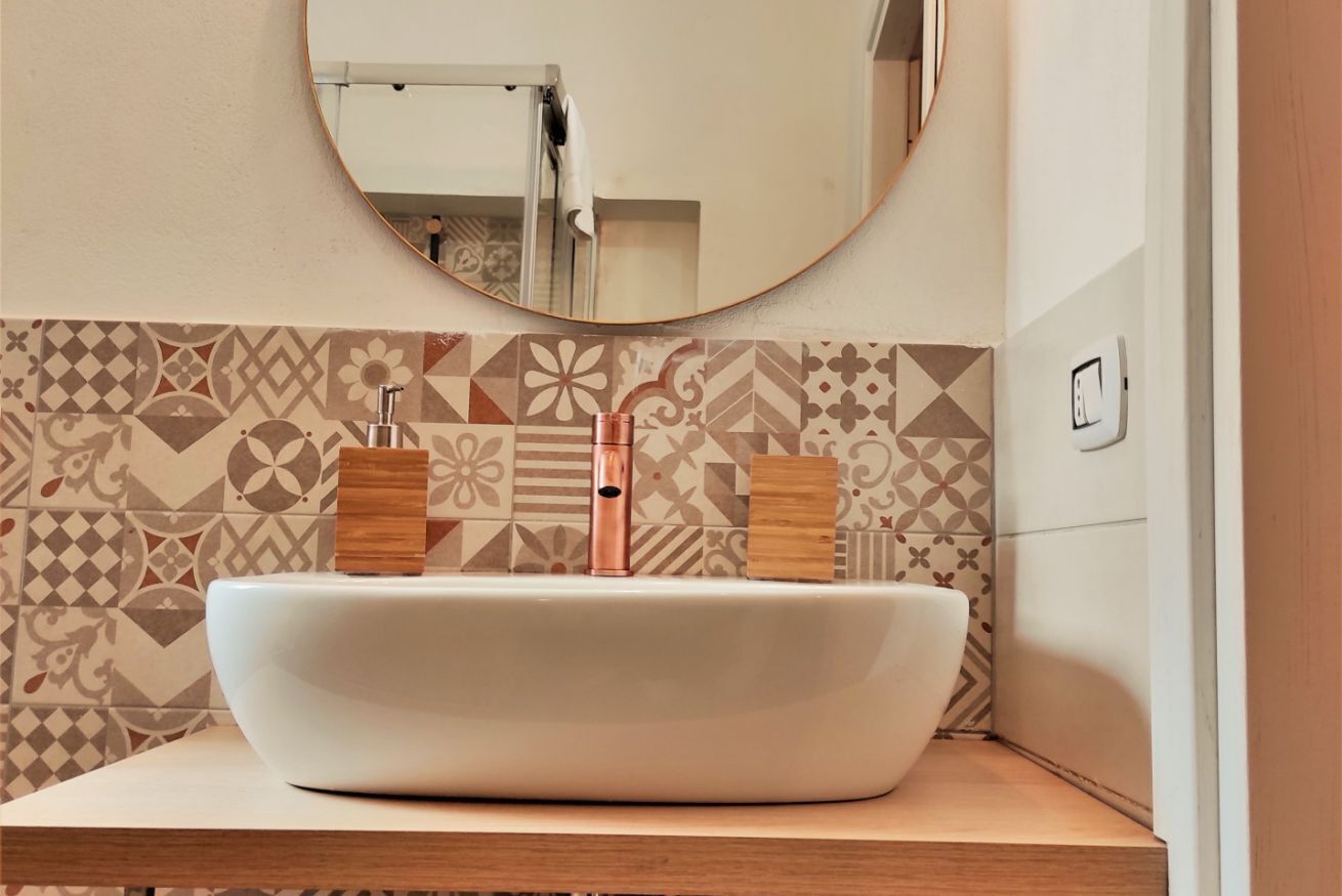 Une salle de bain avec un lavabo sur colonne blanc, des poignées en bois et un pare-baignoire en carreaux à motifs.