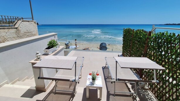 A rooftop terrace with sun loungers, a table with a potted plant, and a view of the beach and ocean. - Perla del Golfo Ortigia Holidays (Fontane Bianche)