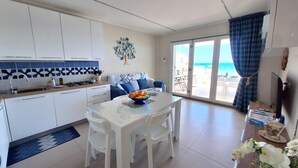 A modern kitchen with white cabinets, a dining table with chairs, and a view of the sea through large glass doors. - Perla del Golfo Ortigia Holidays (Fontane Bianche)