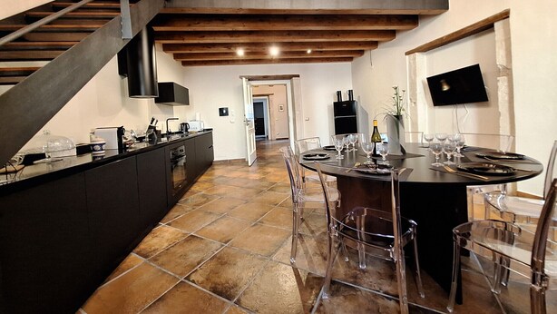 Una cocina moderna con una isla central, un comedor con mesa redonda y una escalera que conduce a un nivel superior.
