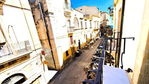 Una calle estrecha flanqueada por edificios, con mesas al aire libre de un café y un cielo azul despejado.