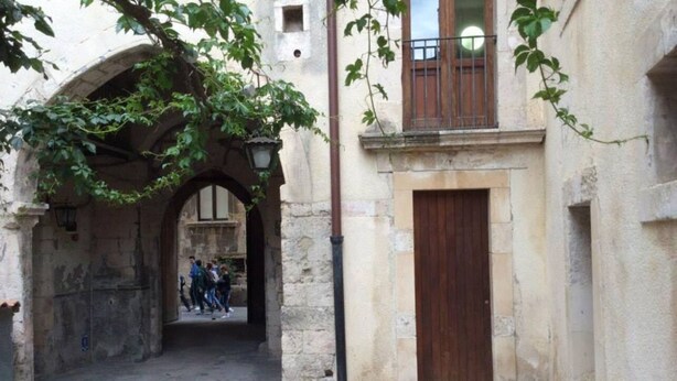 A narrow alleyway with stone walls, a wooden door, and a balcony with a metal railing. - Domus 1333 Ortigia Holidays (Siracusa)