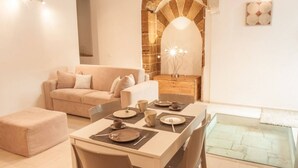 A cozy living area with a dining table set for four, a sofa, and a fireplace with a stone arch. - Domus 1333 Ortigia Holidays (Siracusa)