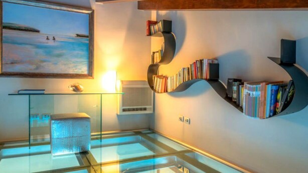 A modern reading room with a glass table, a bookshelf, and a painting of a beach scene. - La Boheme di Ortigia (Siracusa)