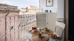 A balcony with a table set for breakfast, including pastries and a cup, with a cityscape view. - La Boheme di Ortigia (Siracusa)