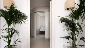 A hallway with two potted plants on either side, leading to a bedroom with a bed and a nightstand. - La Boheme di Ortigia (Siracusa)