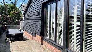 A modern building with large windows and a patio area with a table and chairs. - The Cart Lodge at Lee Wick Farm Cottages (Clacton on Sea)