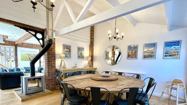 A dining area with a large round table surrounded by chairs, a fireplace, and a staircase leading to another level. - The Cart Lodge at Lee Wick Farm Cottages (Clacton on Sea)