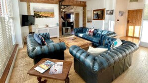 A spacious living room with a large blue leather sofa, a wooden coffee table, and a fireplace. - The Cart Lodge at Lee Wick Farm Cottages (Clacton on Sea)