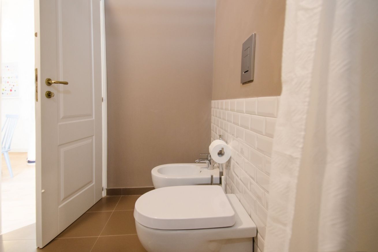 A bathroom with a toilet, bidet, and white tiled walls.