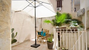 Eine Terrasse mit weißem Sonnenschirm, Holzstühlen und Pflanzen in Töpfen.