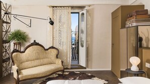 A bedroom with a vintage sofa, a cowhide rug, a bed, a small table with a lamp, and a view of the city through an open door. - Maisonnette V.V.155 Ortigia Holidays (Siracusa)
