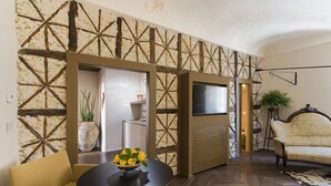 A living room with a stone wall, a sofa, a table with a bowl of lemons, and a TV. - Maisonnette V.V.155 Ortigia Holidays (Siracusa)