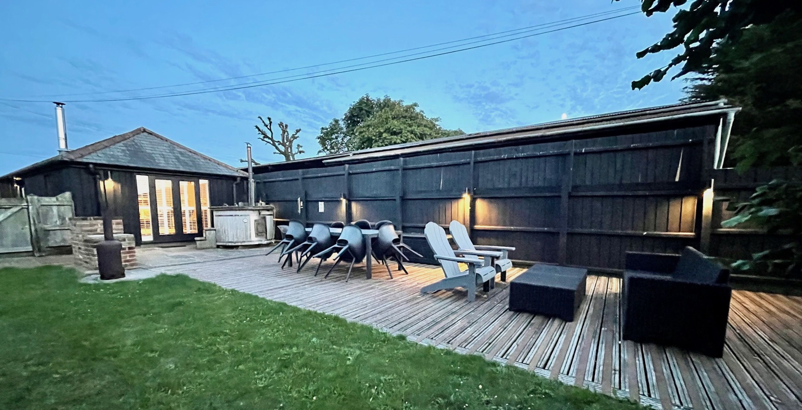 A backyard with a wooden deck, outdoor seating, and a barbecue area.
