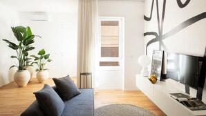 Ein modernes Wohnzimmer mit grauem Sofa, Topfpflanzen, einem Flachbildfernseher und einem großen abstrakten Wandbild.
