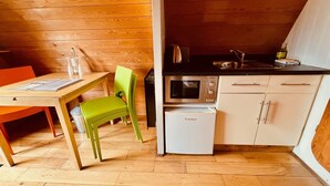 A compact kitchen with wooden walls, a dining table with chairs, a microwave, a small refrigerator, and a sink. - MegaPod 1 at Lee Wick Farm Glamping (Clacton on Sea)