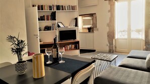 Ein Wohnzimmer mit einer Couch, einem Couchtisch, einem Bücherregal, einem Fernseher und einem Esstisch mit Weingläsern.