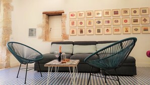 Ein Zimmer mit einer Couch, zwei Sesseln, einem Tisch mit Flasche und Gläsern sowie einer Wand mit gerahmten Bildern.