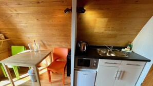 Kompakti keittiö, jossa on puusisustus, ruokapöytä tuoleineen, pesuallas, mikroaaltouuni ja pieni jääkaappi.