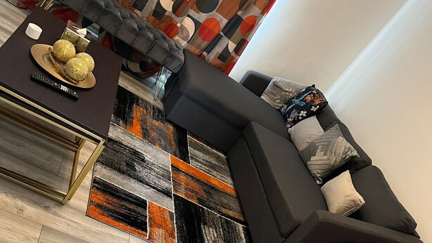 Un salon moderne avec un canapé d’angle, un petit fauteuil orange et un rideau à motifs.
