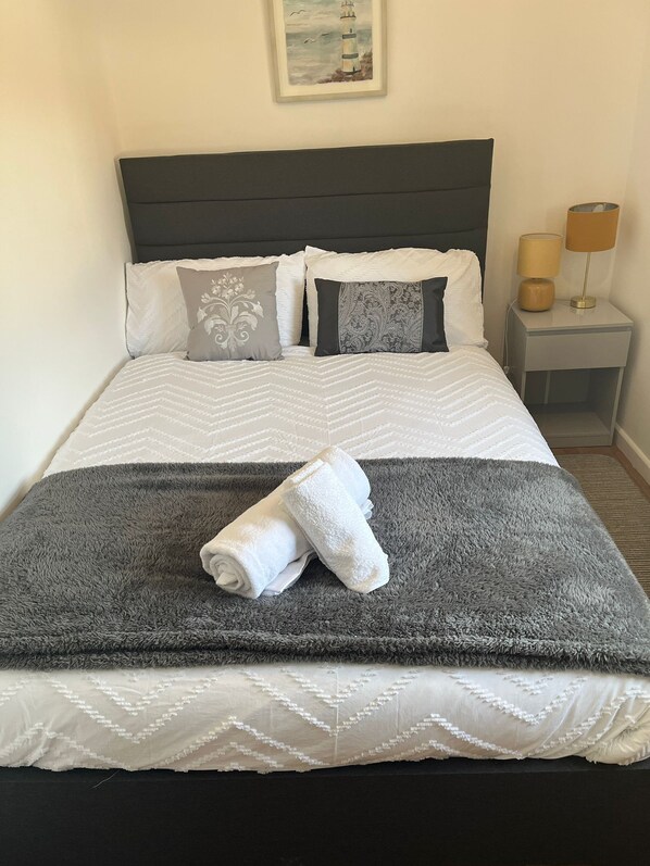 A neatly made bed with a grey and white duvet, pillows, and a rolled white towel.