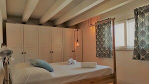 Ein Einzelbett mit Holzrahmen, ein Nachttisch mit Lampe und ein Kleiderschrank mit einem gemusterten Vorhang.