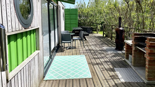 Une terrasse en bois avec un barbecue, des sièges d’extérieur et une porte verte.