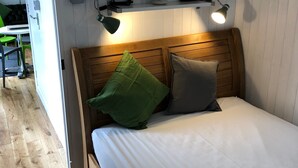 Une chambre à coucher avec une tête de lit en bois, un lit avec une literie blanche, deux oreillers et un luminaire fixé au mur.